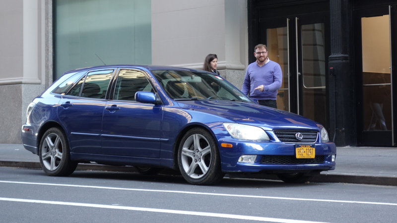 Pictured: My car on a normal, happy day. And me pointing at it like a big dumb goof in a silly purple sweater. The offending tire can be seen, before its untimely demise. I don’t know who that other person is.